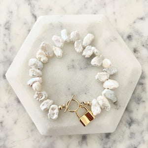 Keishi pearl bracelet with a gold lock charm on marble coaster